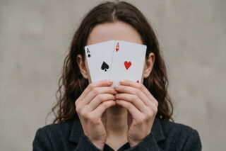 Junge Frau hält zwei Spielkarten vors Gesicht